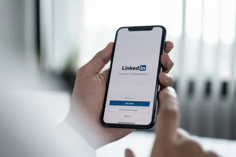 Mão segurando um smartphone com a tela de cadastro do LinkedIn para empresas exibindo os botões "Join now" e "Sign in"