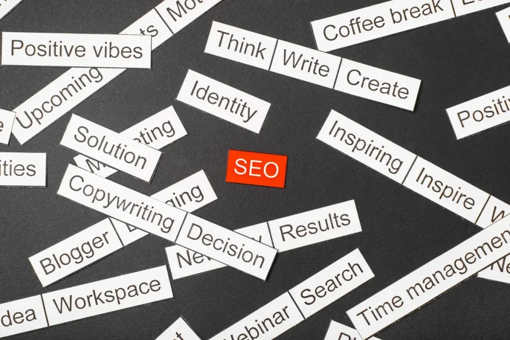 : Etiquetas de papel com palavras de marketing espalhadas ao redor de uma etiqueta vermelha escrita SEO, ilustrando o tema palavras de transição no SEO