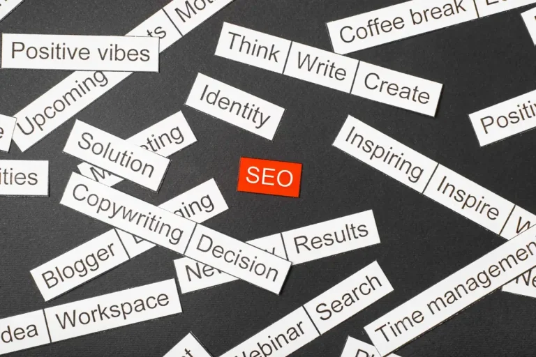 : Etiquetas de papel com palavras de marketing espalhadas ao redor de uma etiqueta vermelha escrita SEO, ilustrando o tema palavras de transição no SEO
