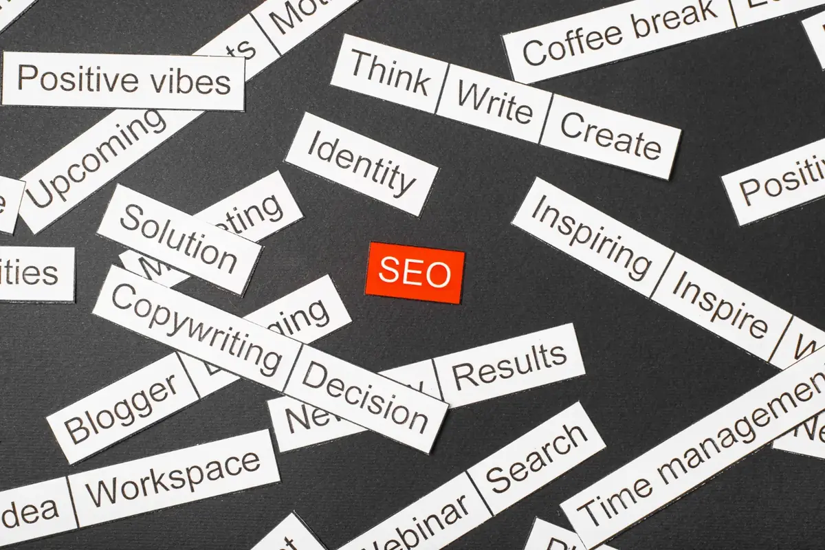 : Etiquetas de papel com palavras de marketing espalhadas ao redor de uma etiqueta vermelha escrita SEO, ilustrando o tema palavras de transição no SEO